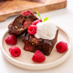 A plated sweet potato brownie with vanilla ice cream and fresh raspberries, with the brownie pan in the background.