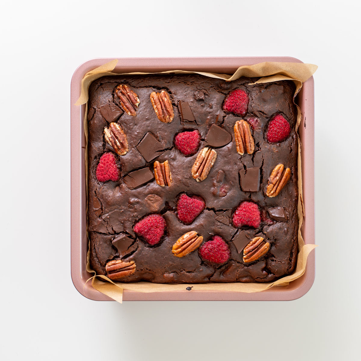 Baked sweet potato brownies in an 8 x 8-inch pan, topped with dark chocolate pieces, pecans, and raspberries.