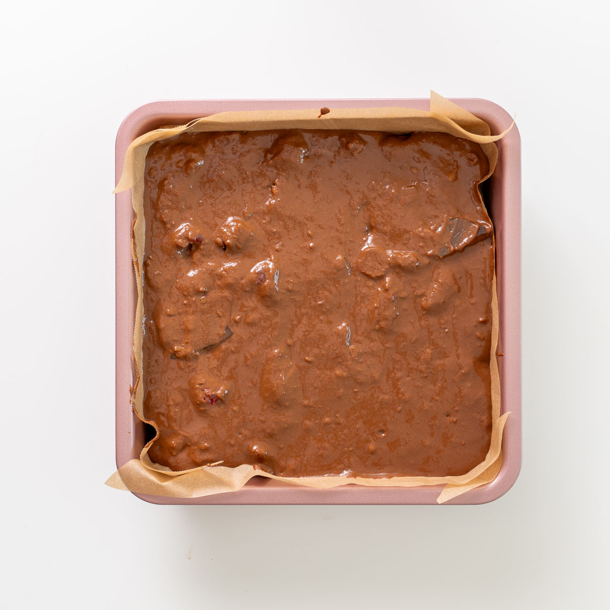 Brownie batter spread into a lined square baking pan before baking.