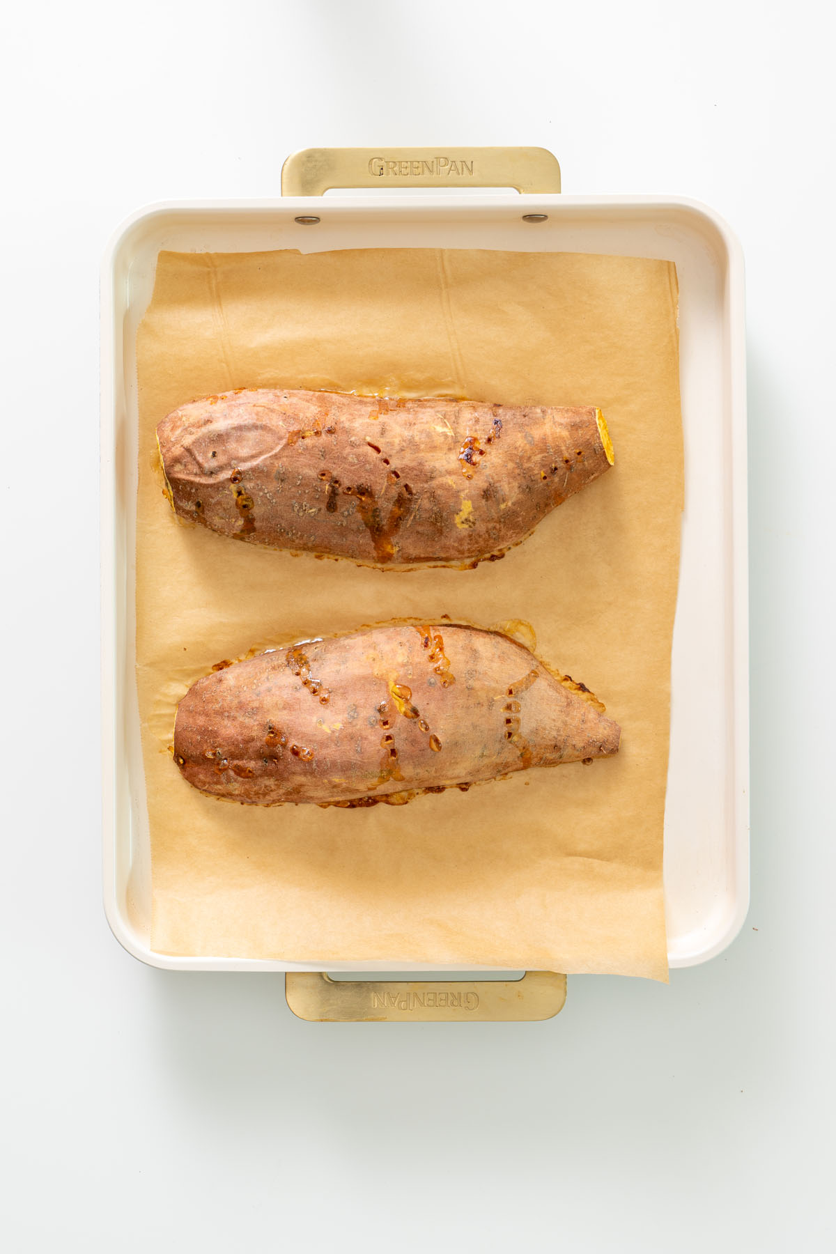 Two baked sweet potatoes on a parchment-lined baking tray after roasting.