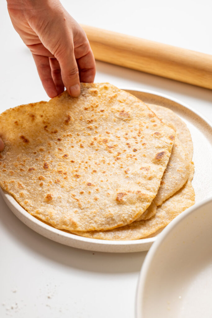 Sarah Cobacho holding a freshly cooked whole wheat wrap from a stack on a plate