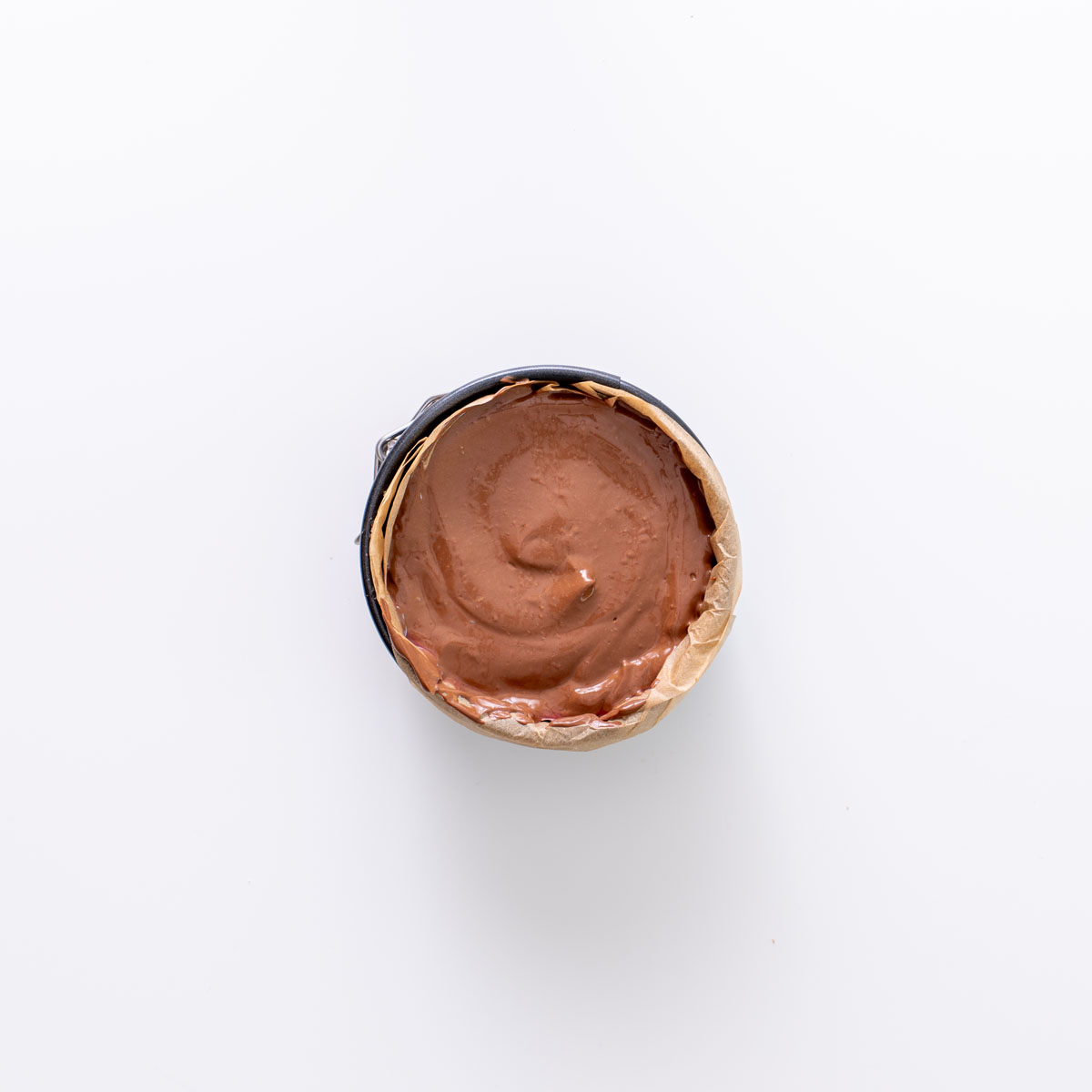 Top-down view of chocolate mousse in a parchment-lined mini tart pan on a white background.