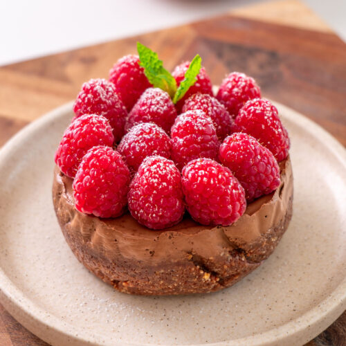 Close-up of a no-bake mini chocolate tart topped with fresh raspberries, powdered sugar, and mint on a plate.