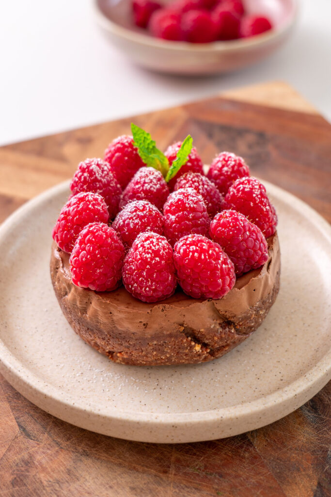 Close-up of a no-bake mini chocolate tart topped with fresh raspberries, powdered sugar, and mint on a plate.