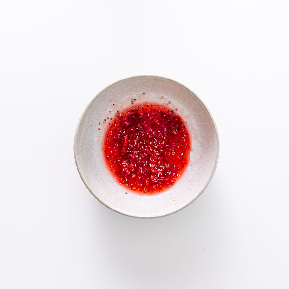Raspberry chia jam mixture in a small bowl on a white background.