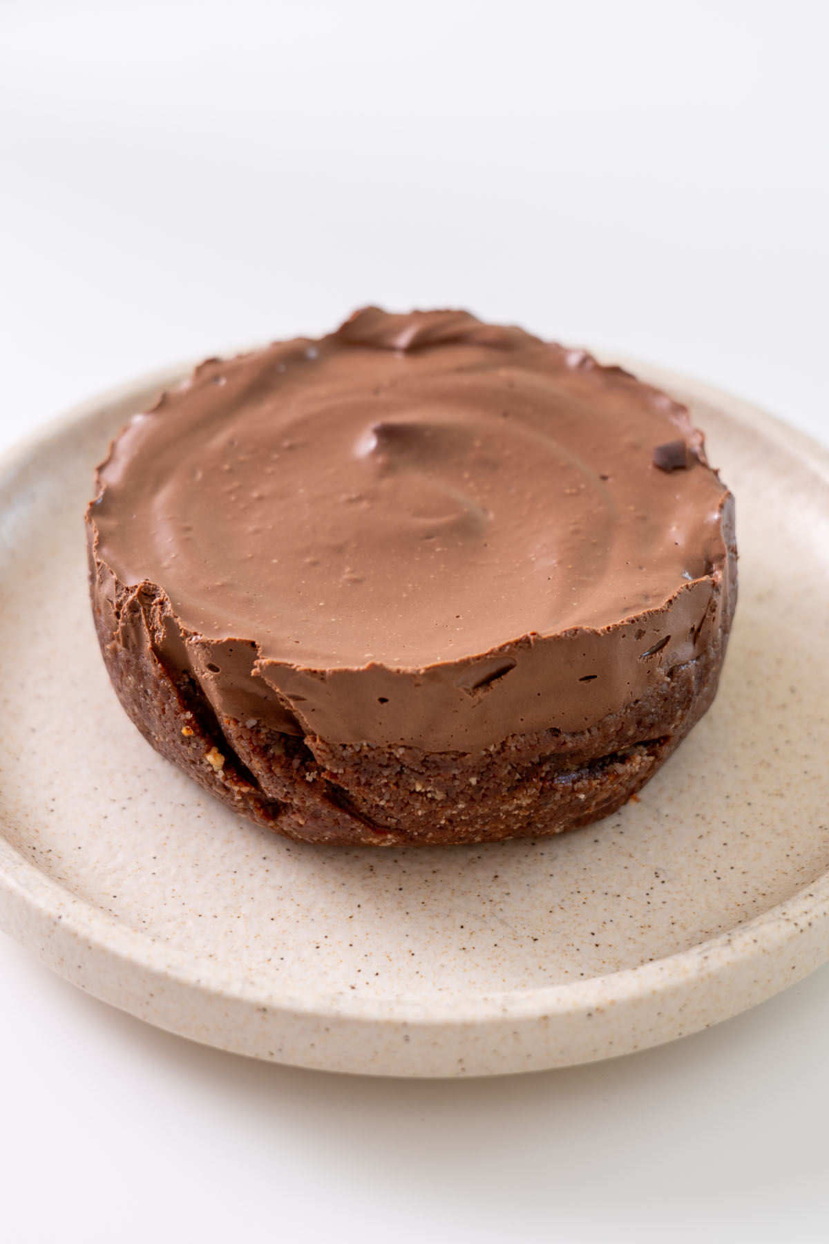 Side view of a no-bake mini chocolate tart with hazelnut cacao crust and smooth chocolate mousse filling on a plate.