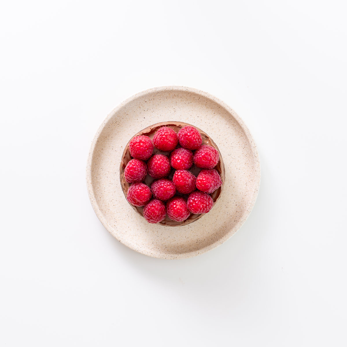 Top-down view of a mini chocolate tart topped with fresh raspberries on a ceramic plate.