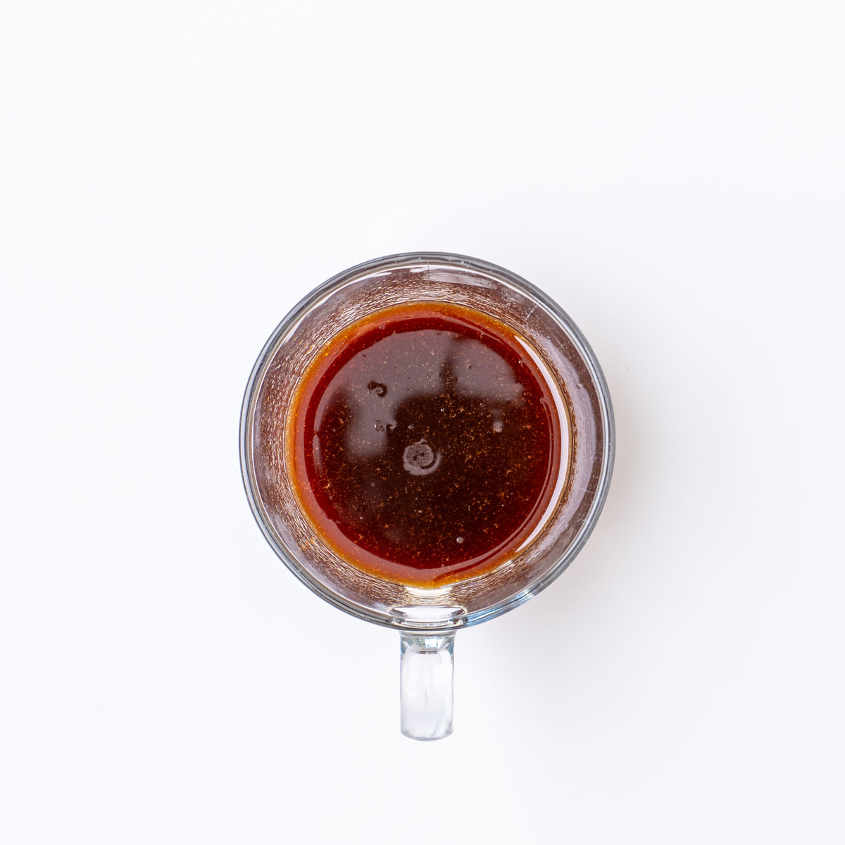 Sticky gochujang sauce mixed in a small glass measuring cup on a white surface