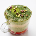 Matcha tiramisu overnight oats in a glass mug topped with matcha powder and chopped pistachios