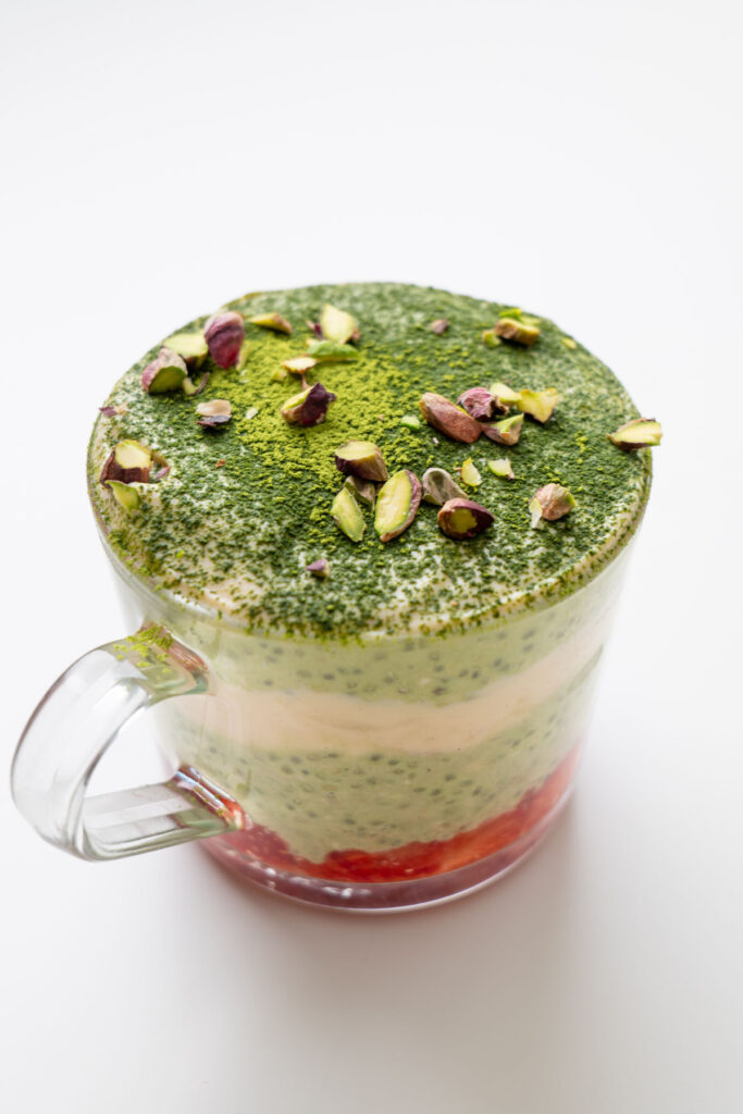 Matcha tiramisu overnight oats in a glass mug topped with matcha powder and chopped pistachios