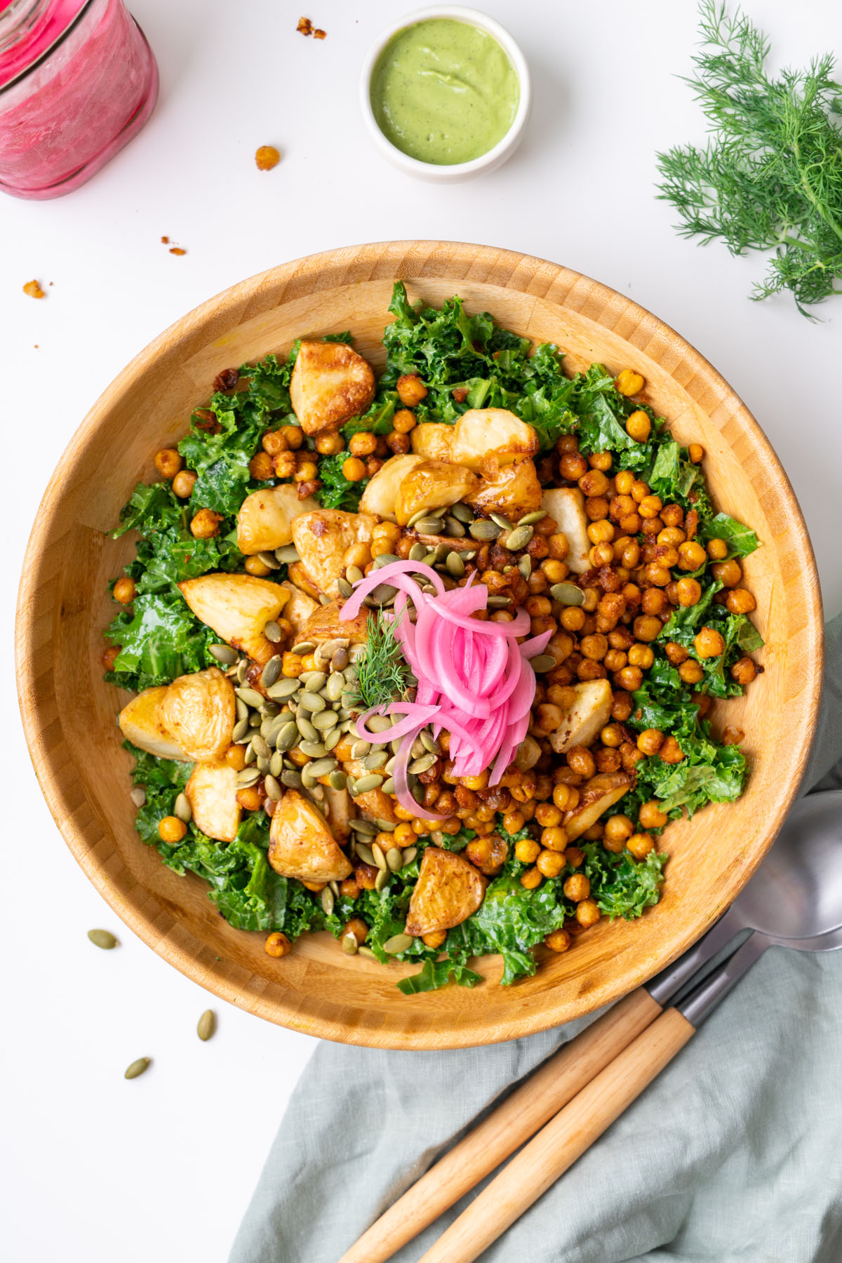 Overhead view of roasted potato and avocado ranch salad in a wooden bowl topped with crispy chickpeas, pumpkin seeds, pickled red onion, and fresh dill, with avocado ranch dressing on the side