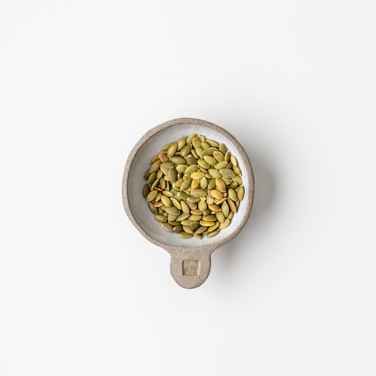 Pumpkin seeds in a small ceramic dish on a white surface