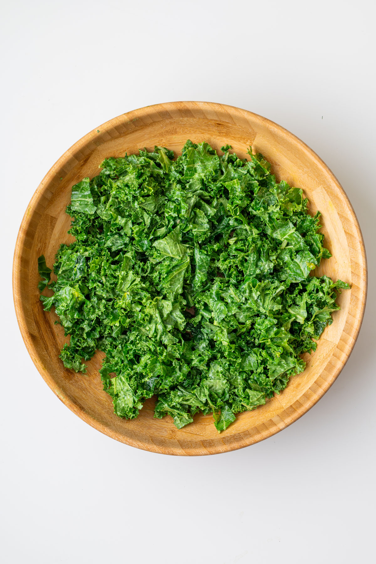 Finely chopped fresh kale in a large wooden serving bowl on a white surface