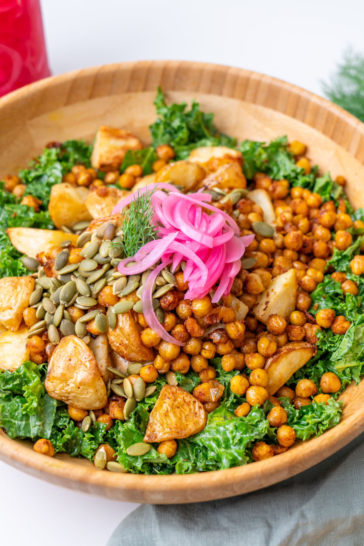 Close-up of roasted potato and avocado ranch salad with crispy chickpeas, pumpkin seeds, pickled red onion, and fresh dill in a wooden bowl