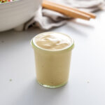 Jar of creamy cashew Caesar dressing on a white surface with a salad bowl in the background.