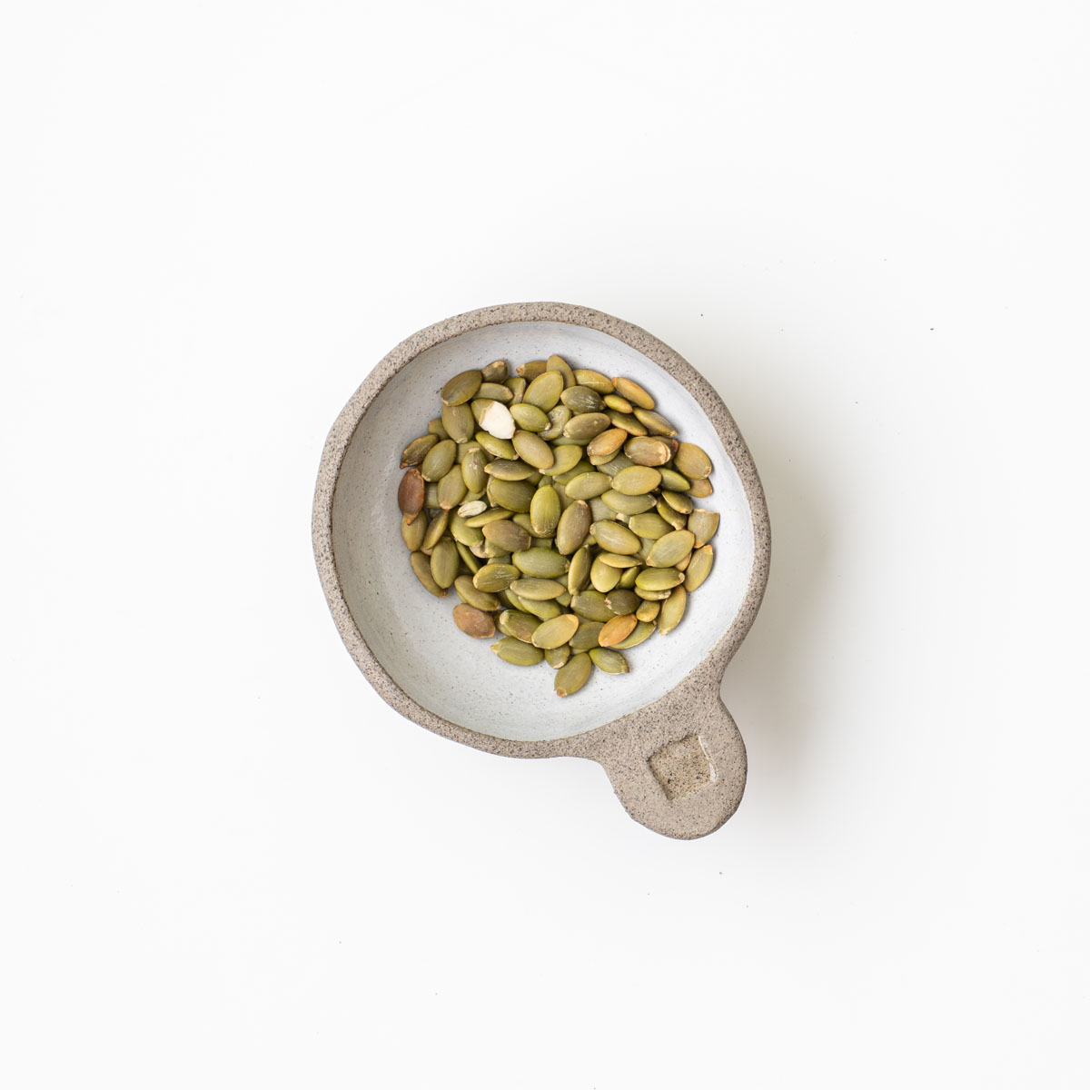 Pepitas in a small ceramic cup used as a topping for a high-protein beetroot medi bowl