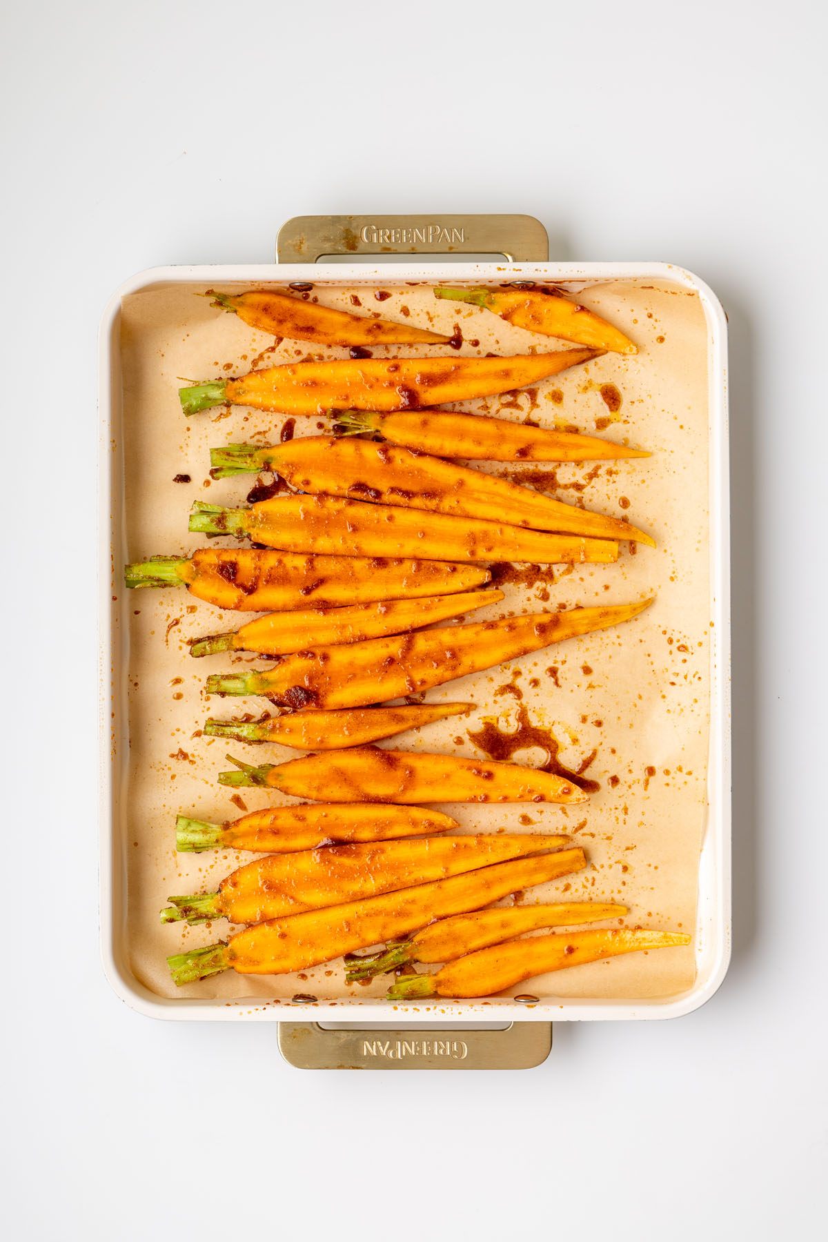 Seasoned dutch carrots with maple syrup and spices on a parchment-lined baking tray ready to roast