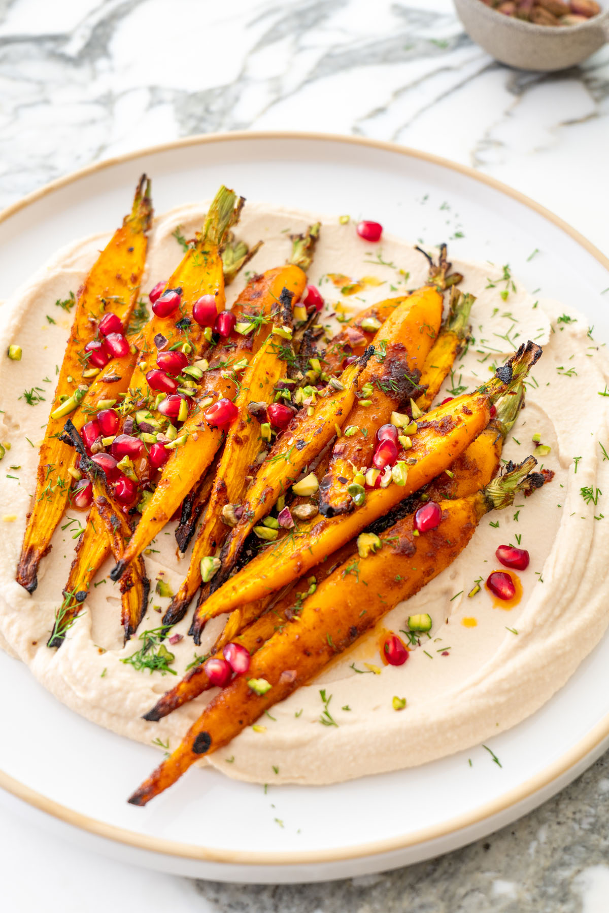 Close-up of maple roasted carrots on creamy butter bean dip with pomegranate seeds, chopped pistachios, and fresh dill