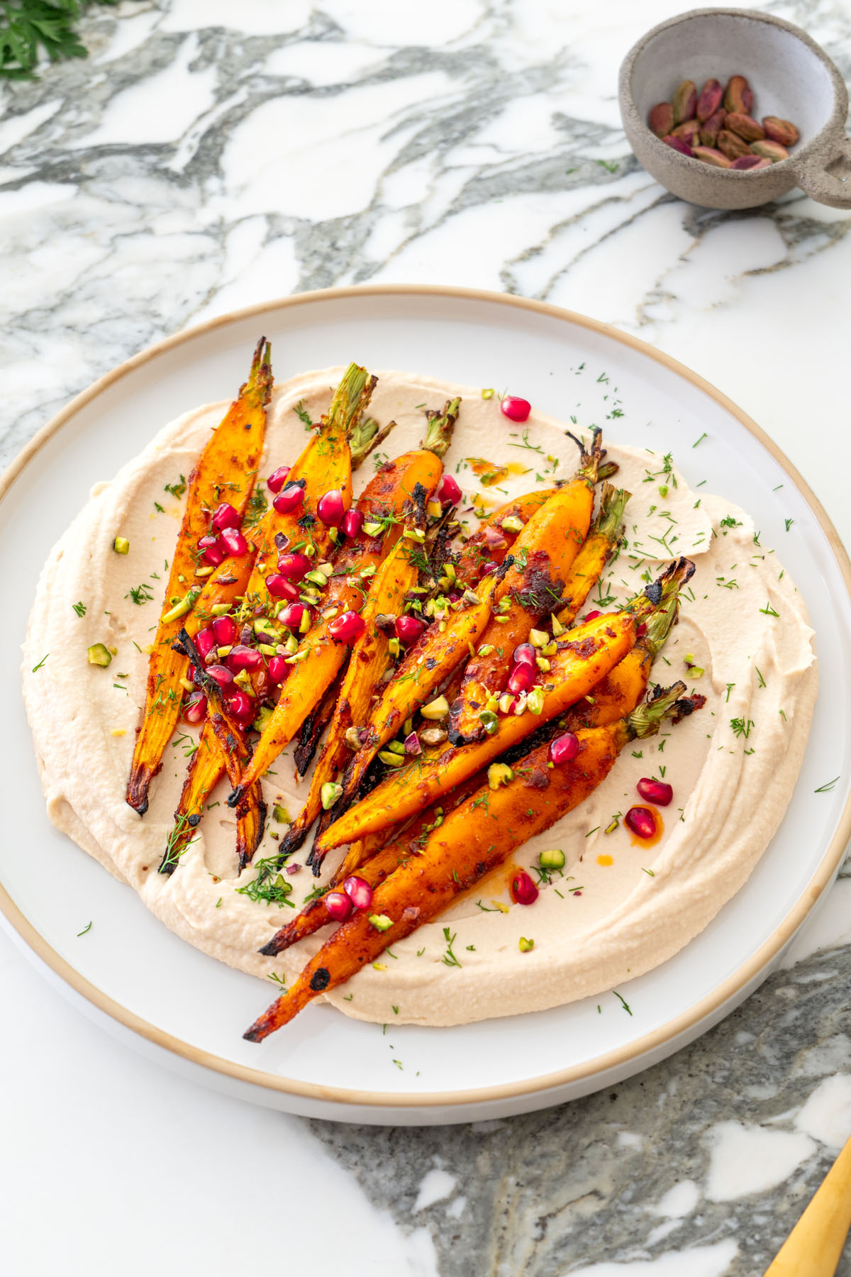 Maple roasted carrots with creamy butter bean dip garnished with pomegranate seeds, pistachios, and dill on a plate