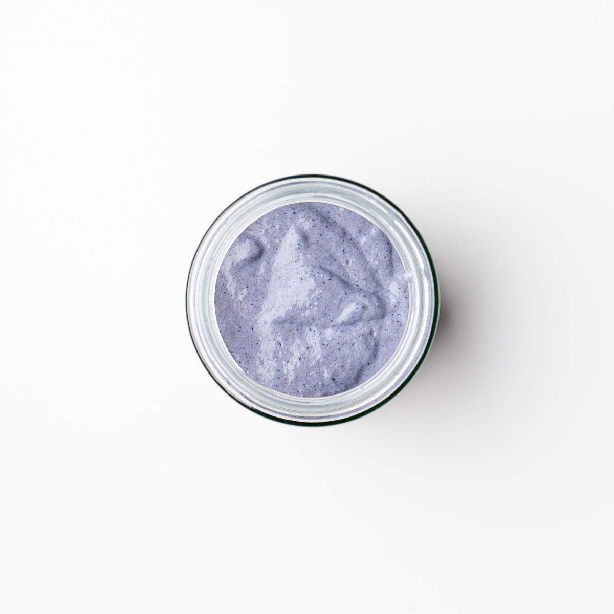 Top-down view of creamy blended blueberry oats in a glass jar before topping, with a soft purple color from the blueberries and chia seeds