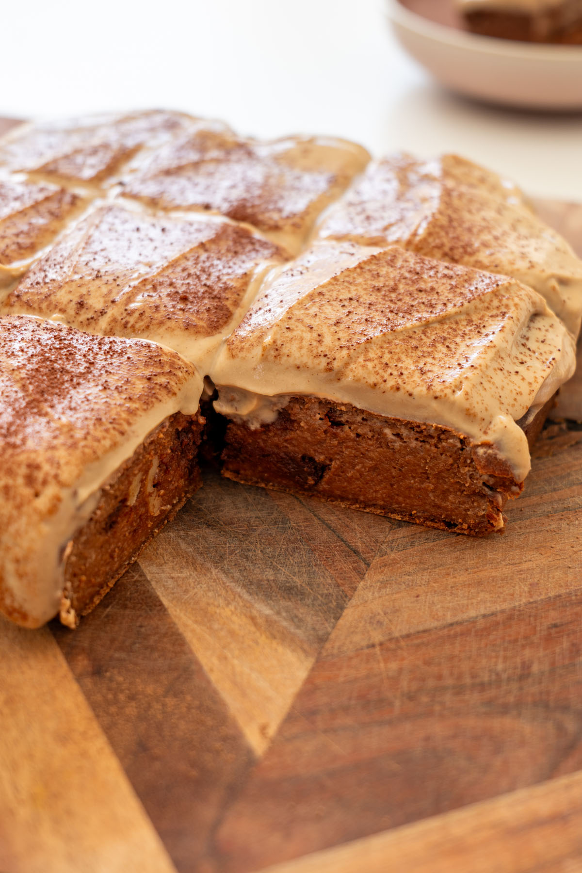 Close-up of brownie baked oats sliced on a wooden board, showing the fudgy chocolate cross-section and creamy coffee yogurt icing on top.