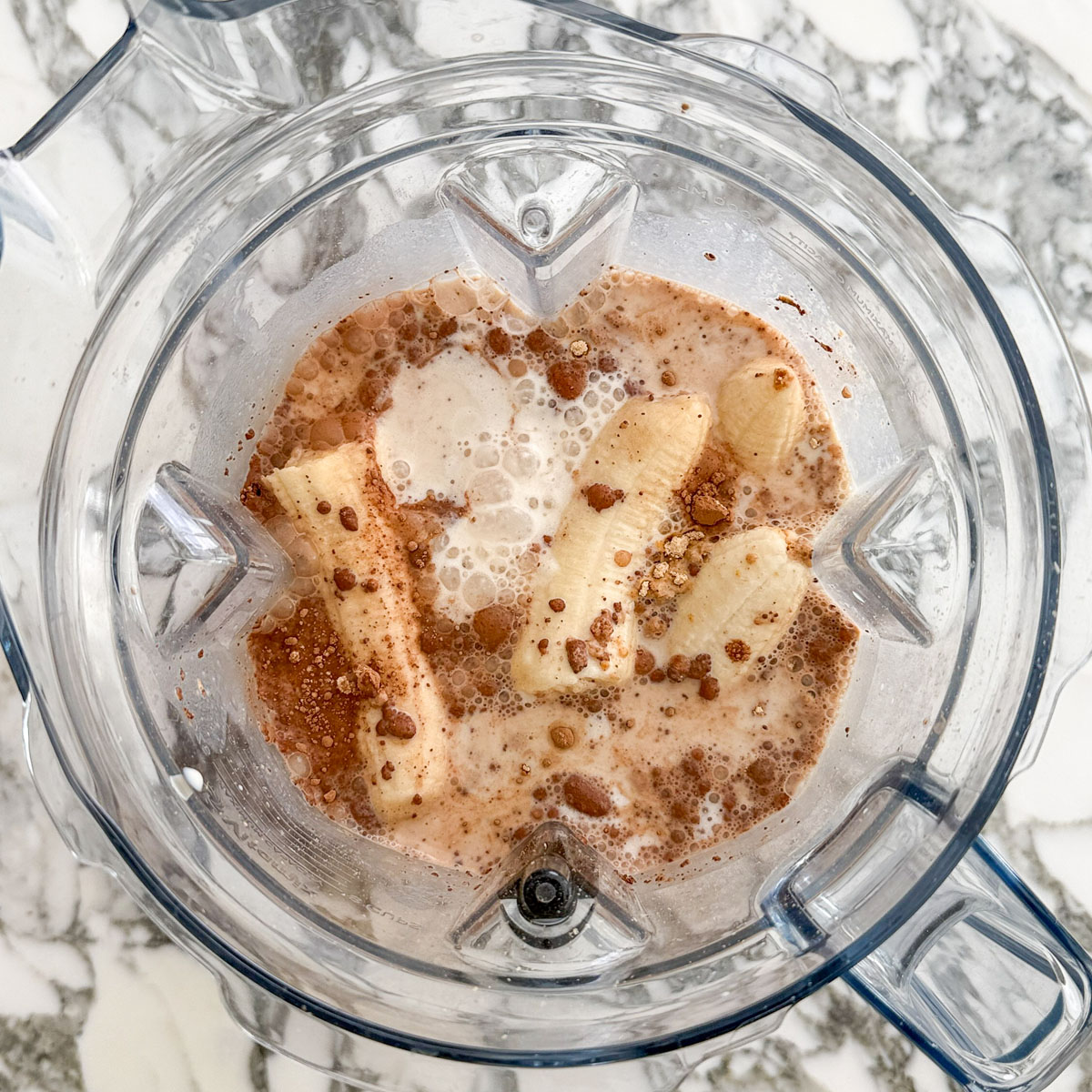 Bananas, rolled oats, raw cacao powder, ground flaxseed, peanut powder, and soy milk in a blender, ready to be blended into the brownie baked oats batter.