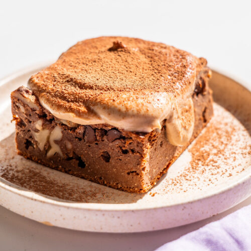 Single slice of brownie baked oats with melting coffee yogurt icing dusted with cacao powder, on a speckled ceramic plate.