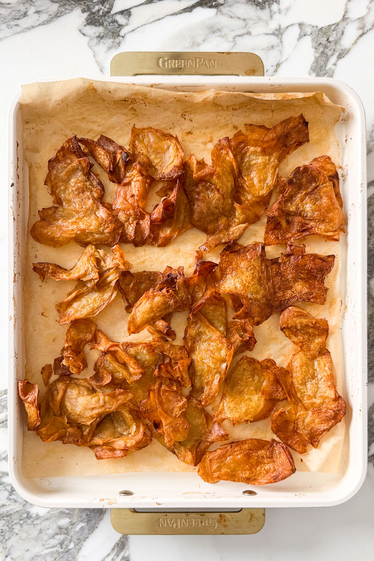 Crispy oven-baked shaved potato slices on a parchment-lined tray, golden and crackly after roasting with smoked paprika and garlic powder