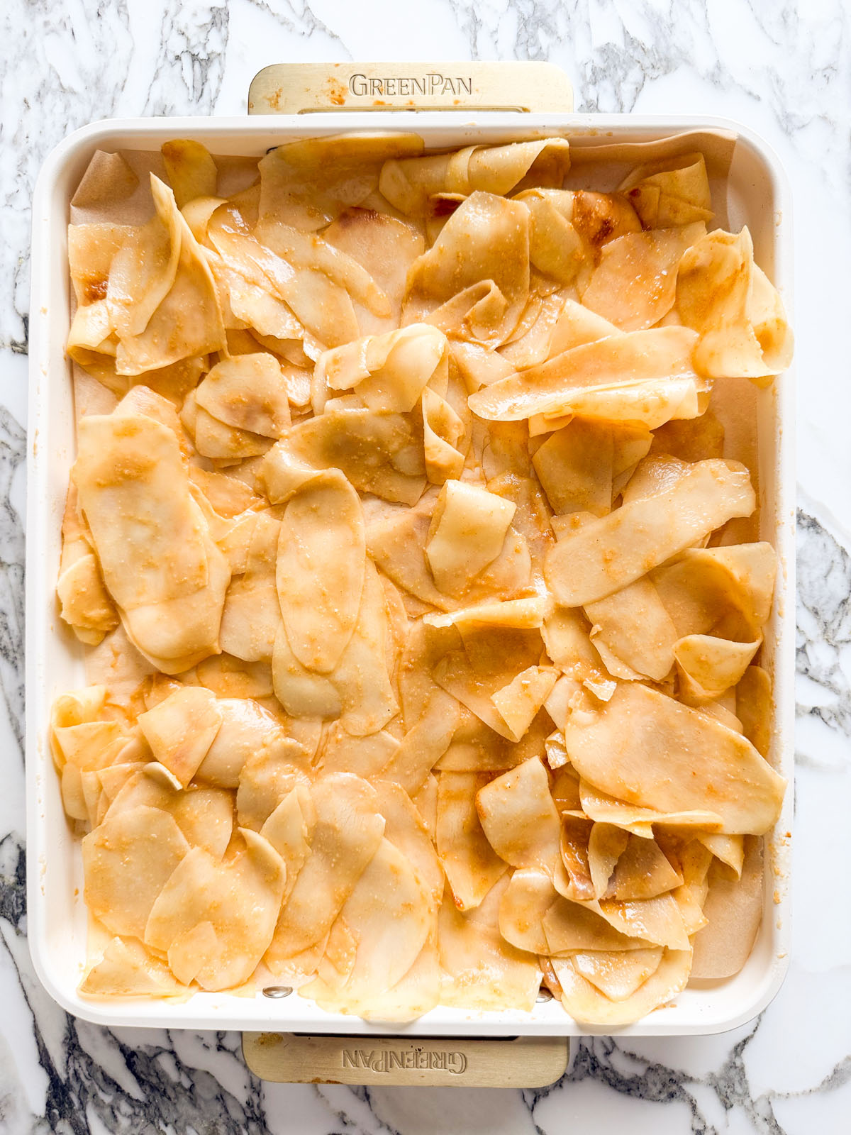Thinly shaved raw potato slices tossed with smoked paprika, garlic powder, and olive oil, spread across a parchment-lined baking tray before baking