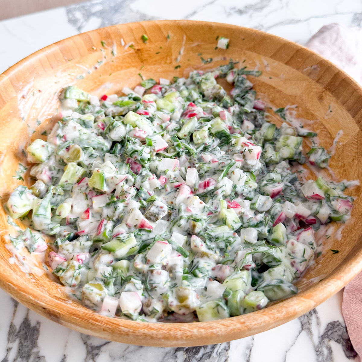 Chopped salad mixture of cucumber, pink radishes, scallions, and fresh dill in a wooden bowl, ready to be tossed with the creamy yogurt-pickle dressing