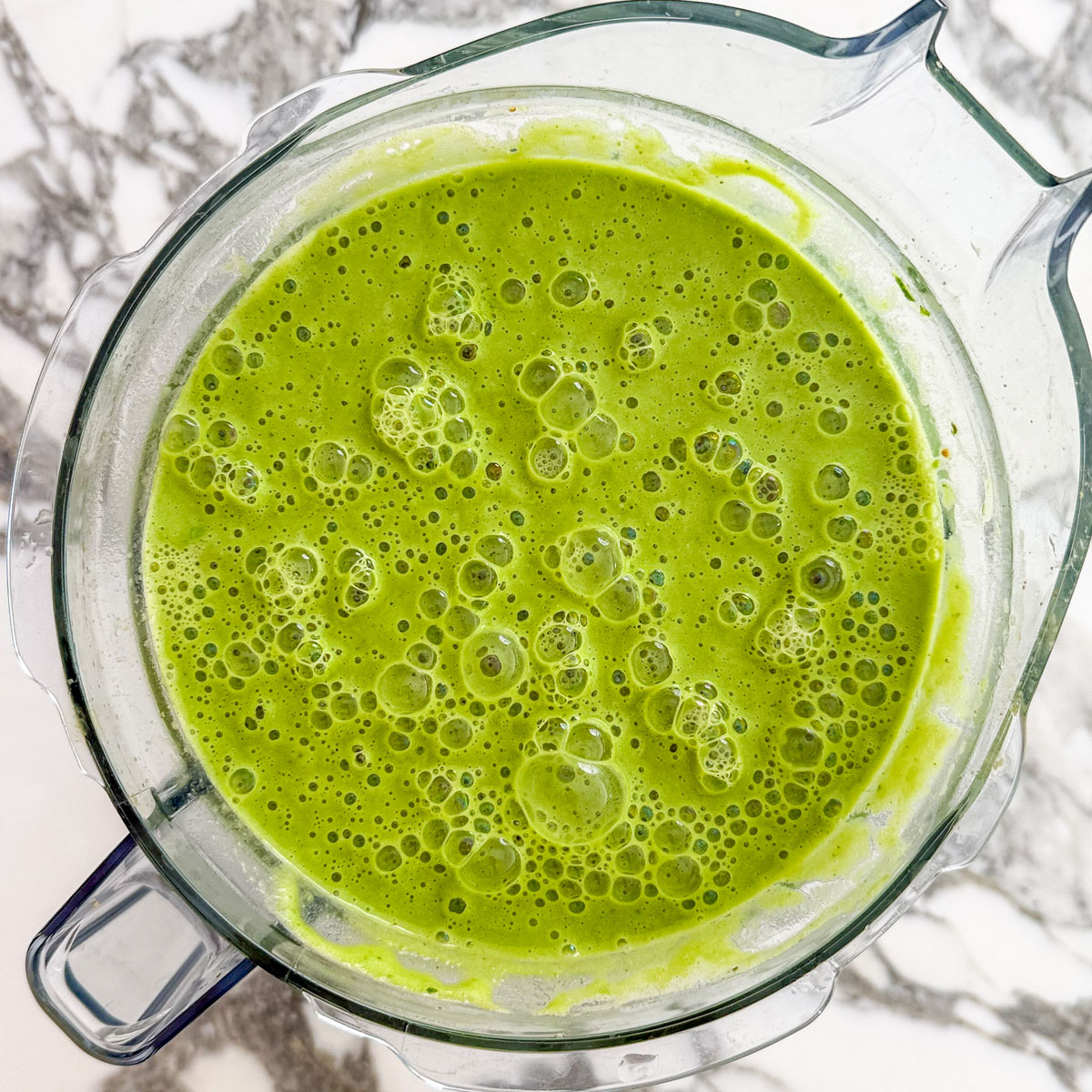 Smooth blended sweet pea and mint soup in a clear blender pitcher on a marble surface
