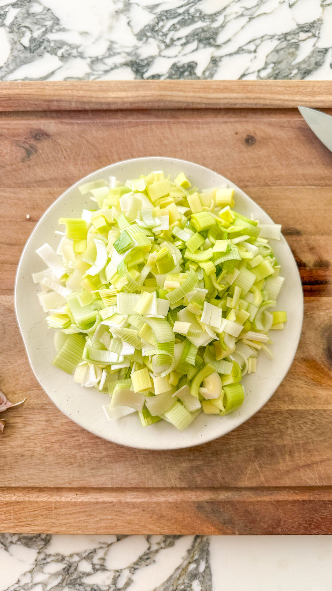 Finely sliced leek on a wooden cutting board on a marble surface, ready to be sauteed for sweet pea soup