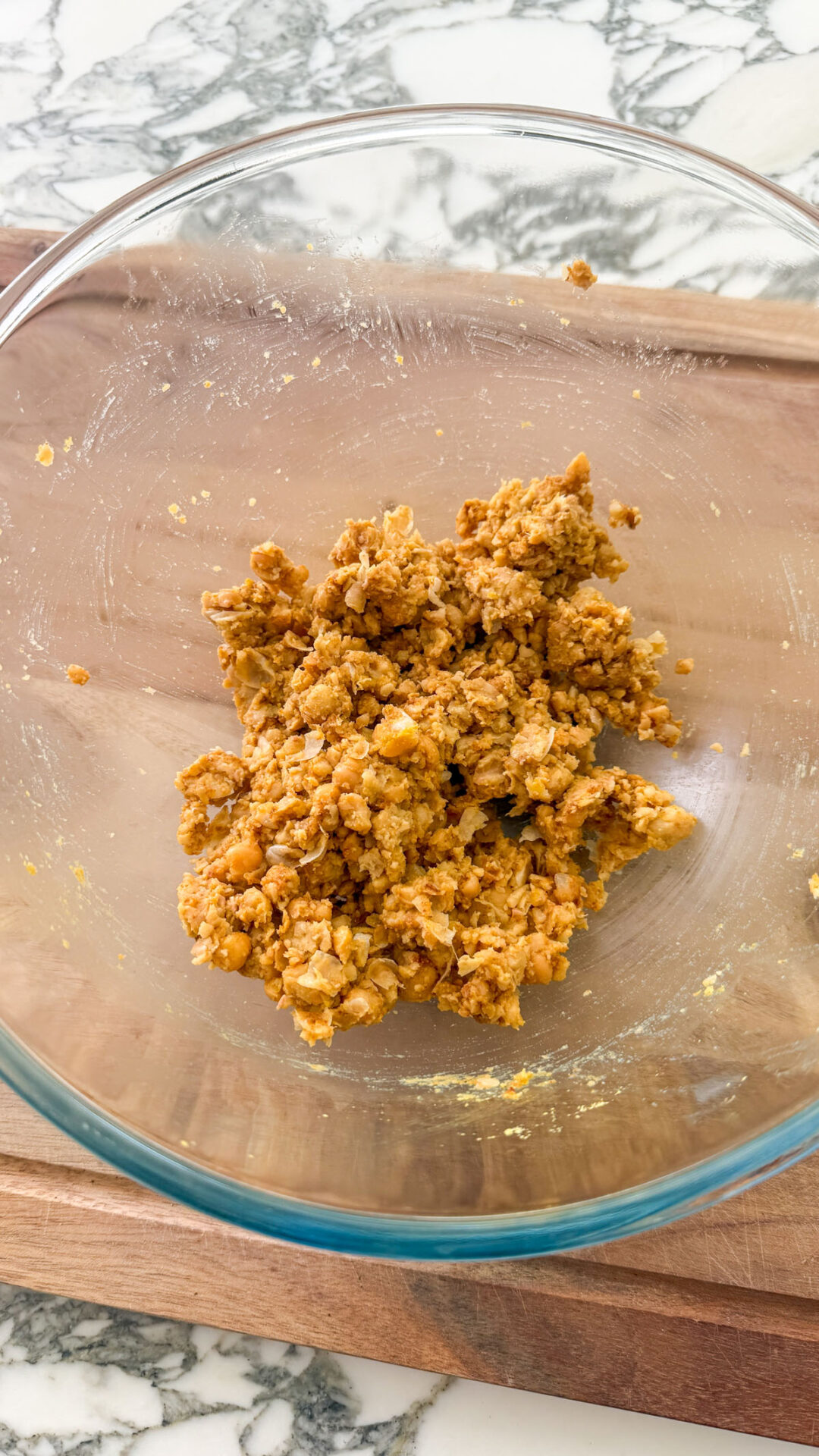 Roughly smashed chickpeas seasoned with smoked paprika, maple syrup, and nutritional yeast in a glass bowl on a wooden cutting board