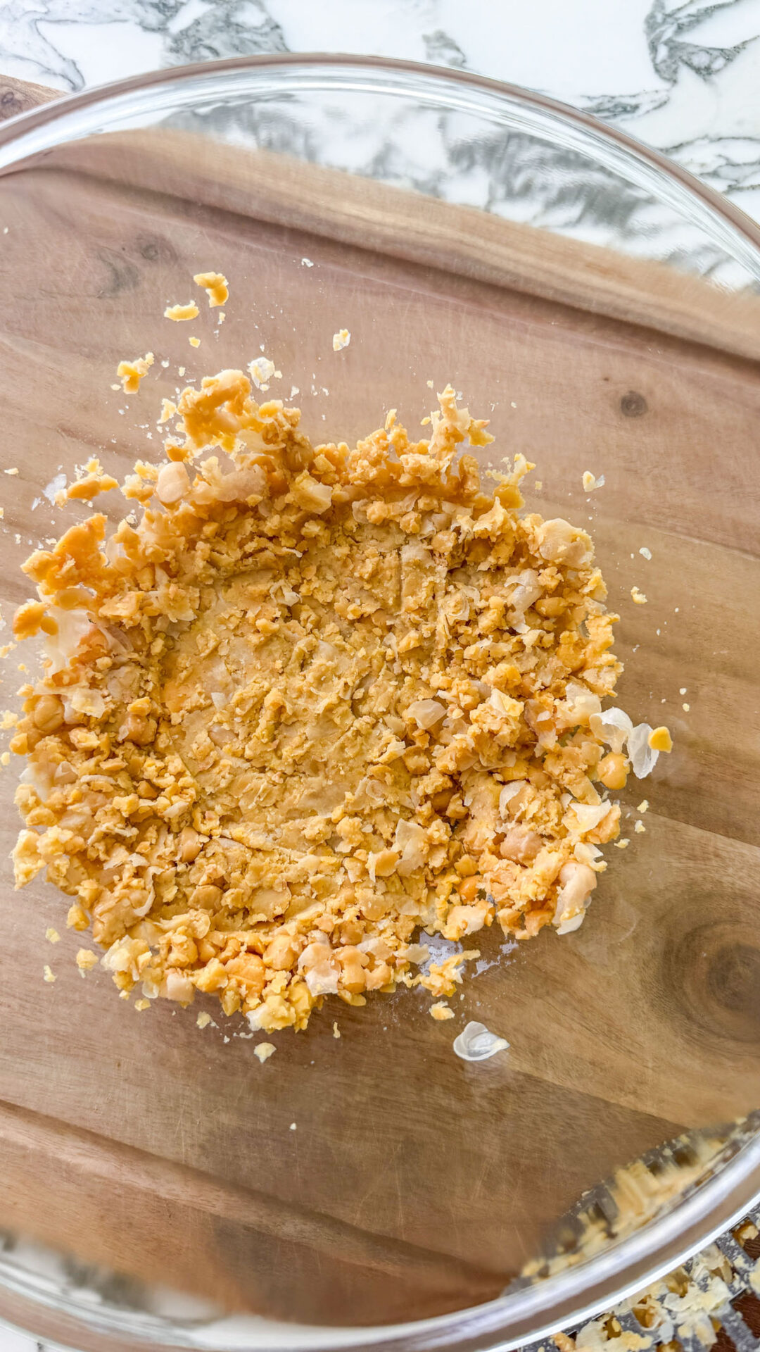 Roughly smashed chickpeas in a glass bowl on a wooden cutting board, ready to be seasoned for the chickpea crumble