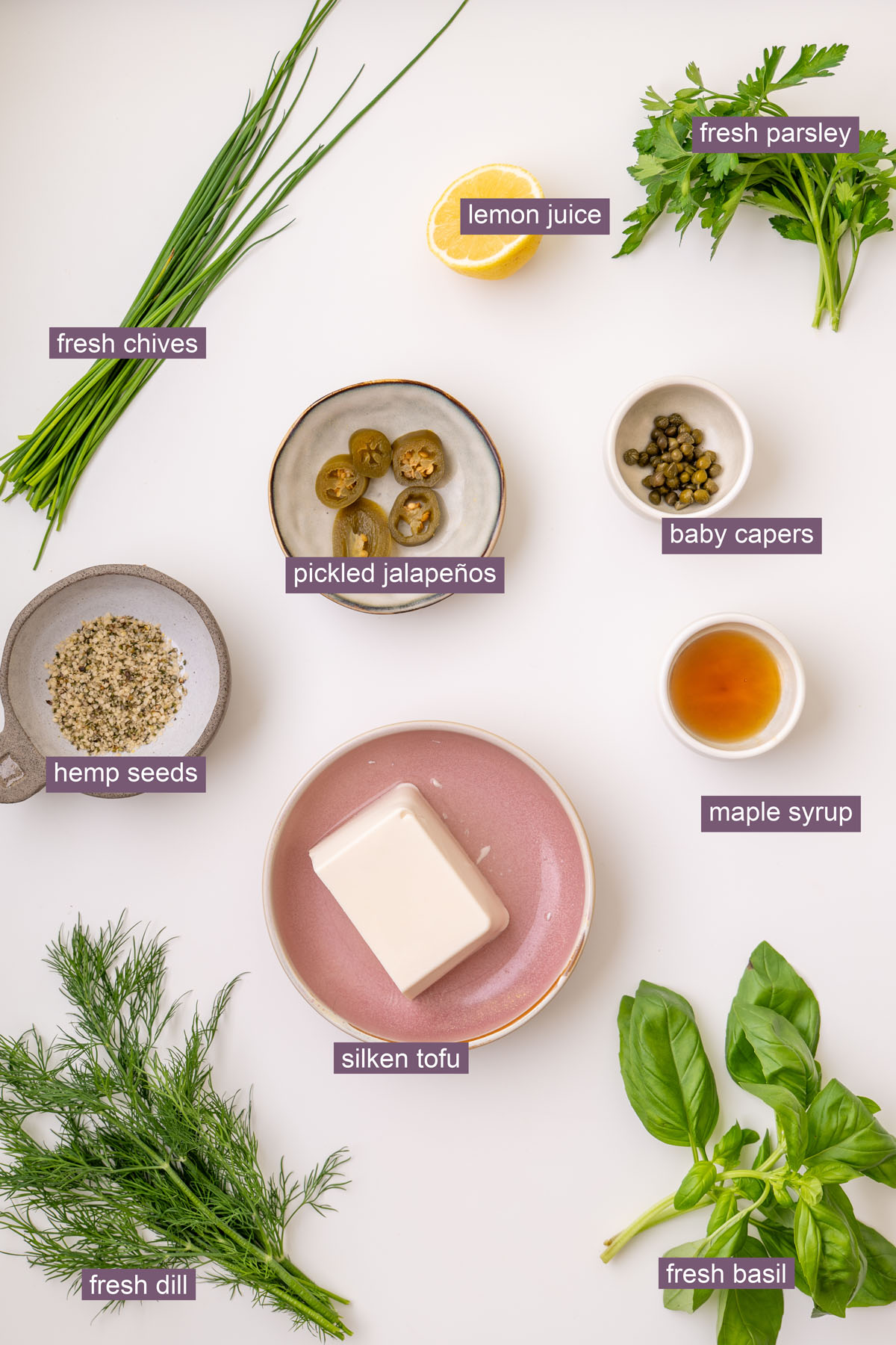 Labeled ingredients for green goddess dressing, including fresh dill, fresh basil, silken tofu, hemp seeds, pickled jalapeños, capers, lemon juice, maple syrup, and fresh herbs.