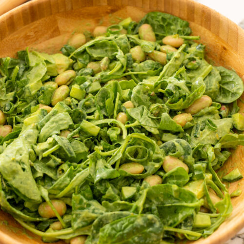 Green salad tossed with green goddess dressing in a wooden bowl