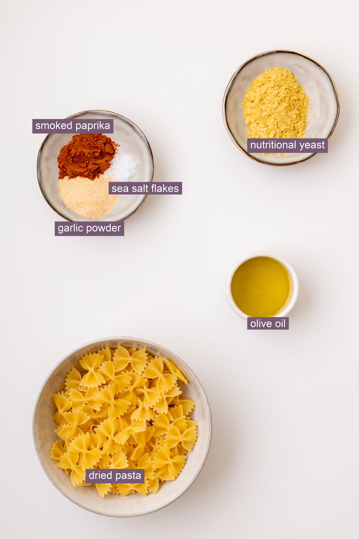 Labeled ingredients for crispy pasta, including dried bowtie pasta, olive oil, nutritional yeast, smoked paprika, garlic powder, and sea salt flakes.