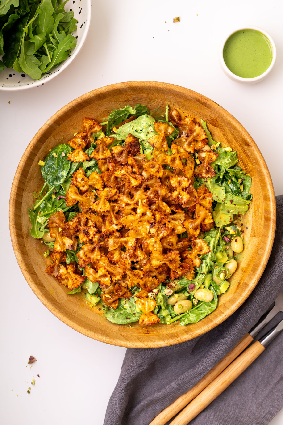 A wooden bowl of viral crispy pasta salad topped with golden crispy pasta, greens, chickpeas, avocado, pistachios, and green goddess dressing.
