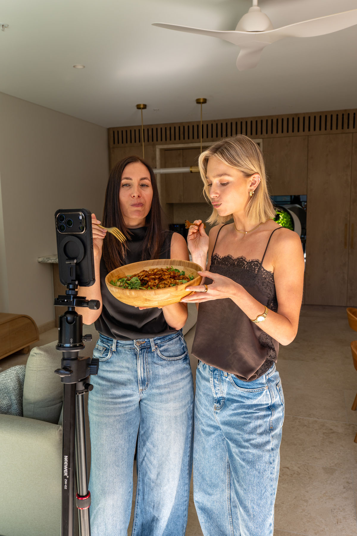 Two people filming and tasting viral crispy pasta salad in a kitchen, with the salad served in a wooden bowl.