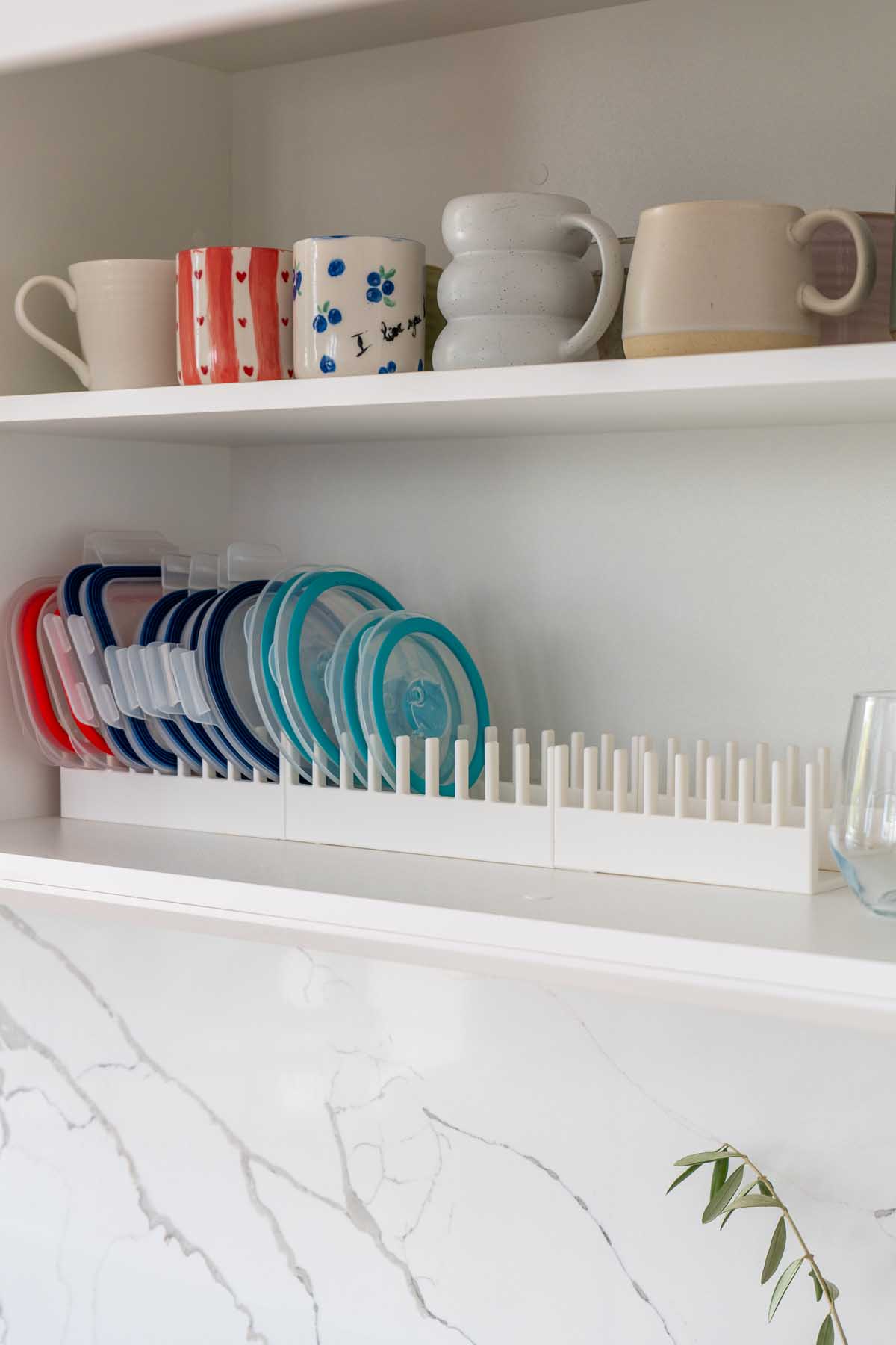 A 3D printed lid organizer on a kitchen shelf holding colored container lids upright and separated by size