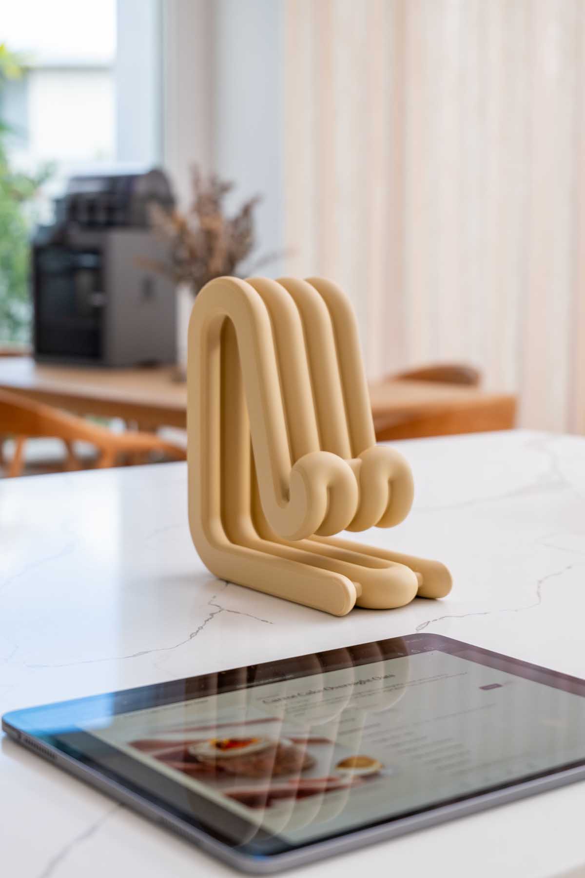 A 3D printed stand propping up a tablet on a kitchen bench, displaying a recipe while cooking