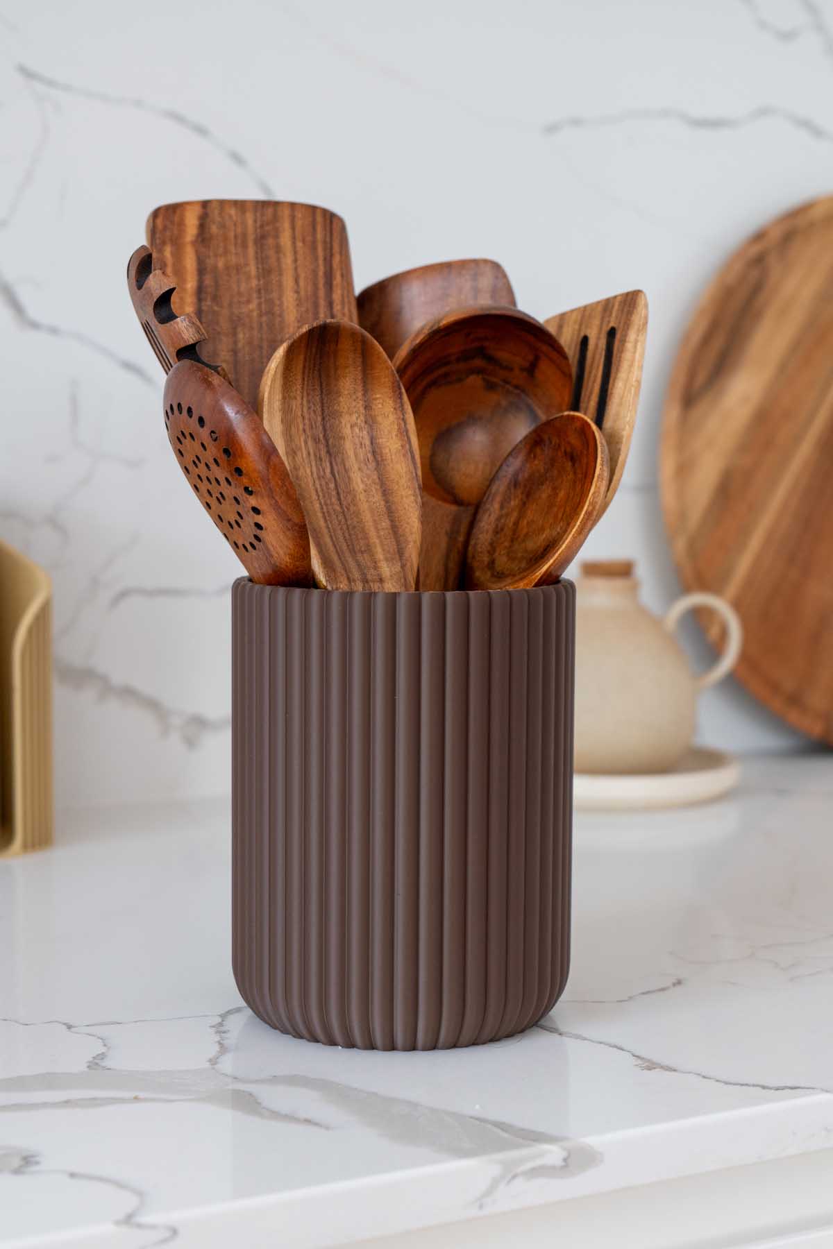 A fluted 3D printed utensil crock on a kitchen bench holding wooden spoons and spatulas