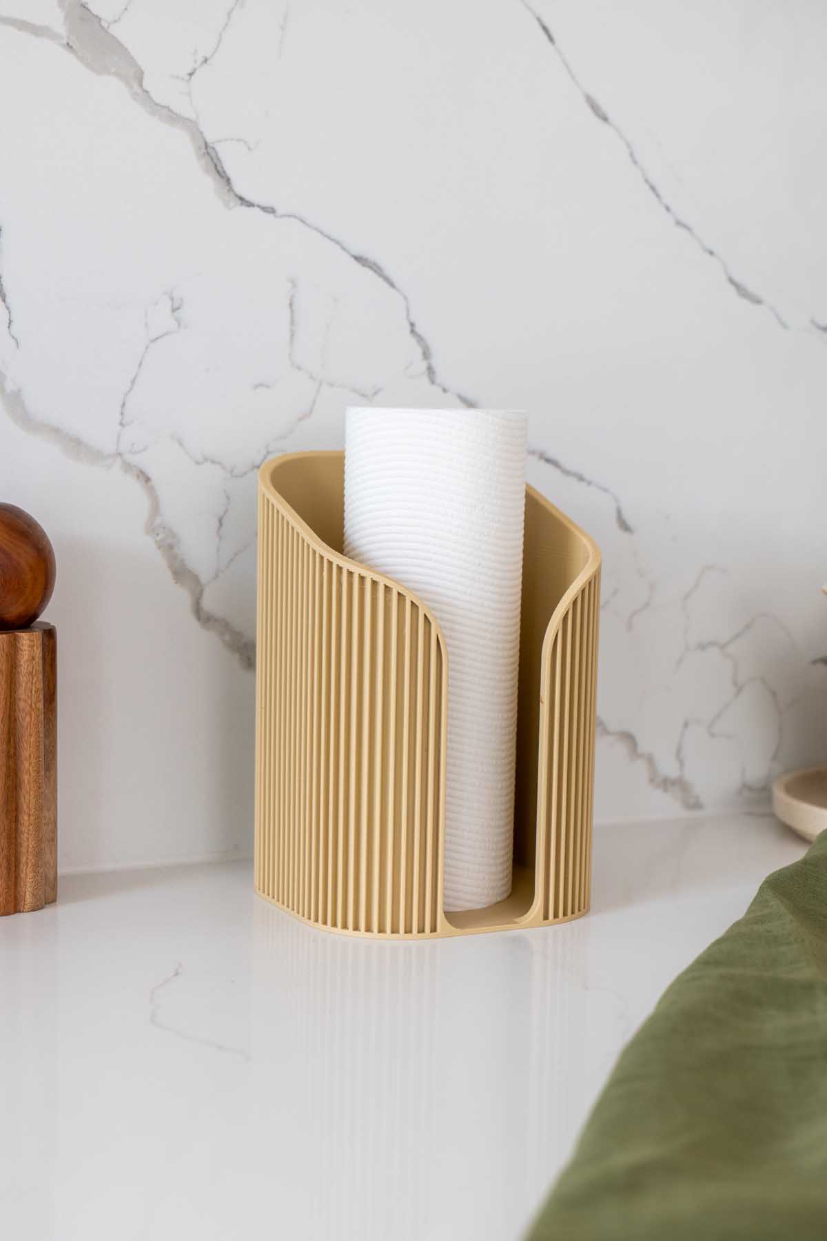 A fluted 3D printed paper towel holder on a kitchen bench with a roll of paper towel on it