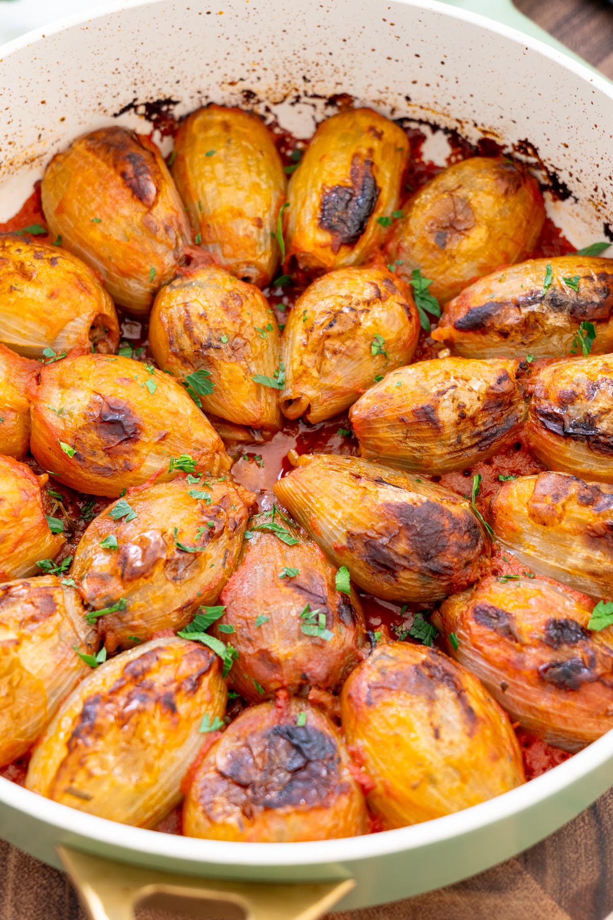 Mediterranean stuffed onions in a pan of tomato sauce, topped with chopped fresh parsley.