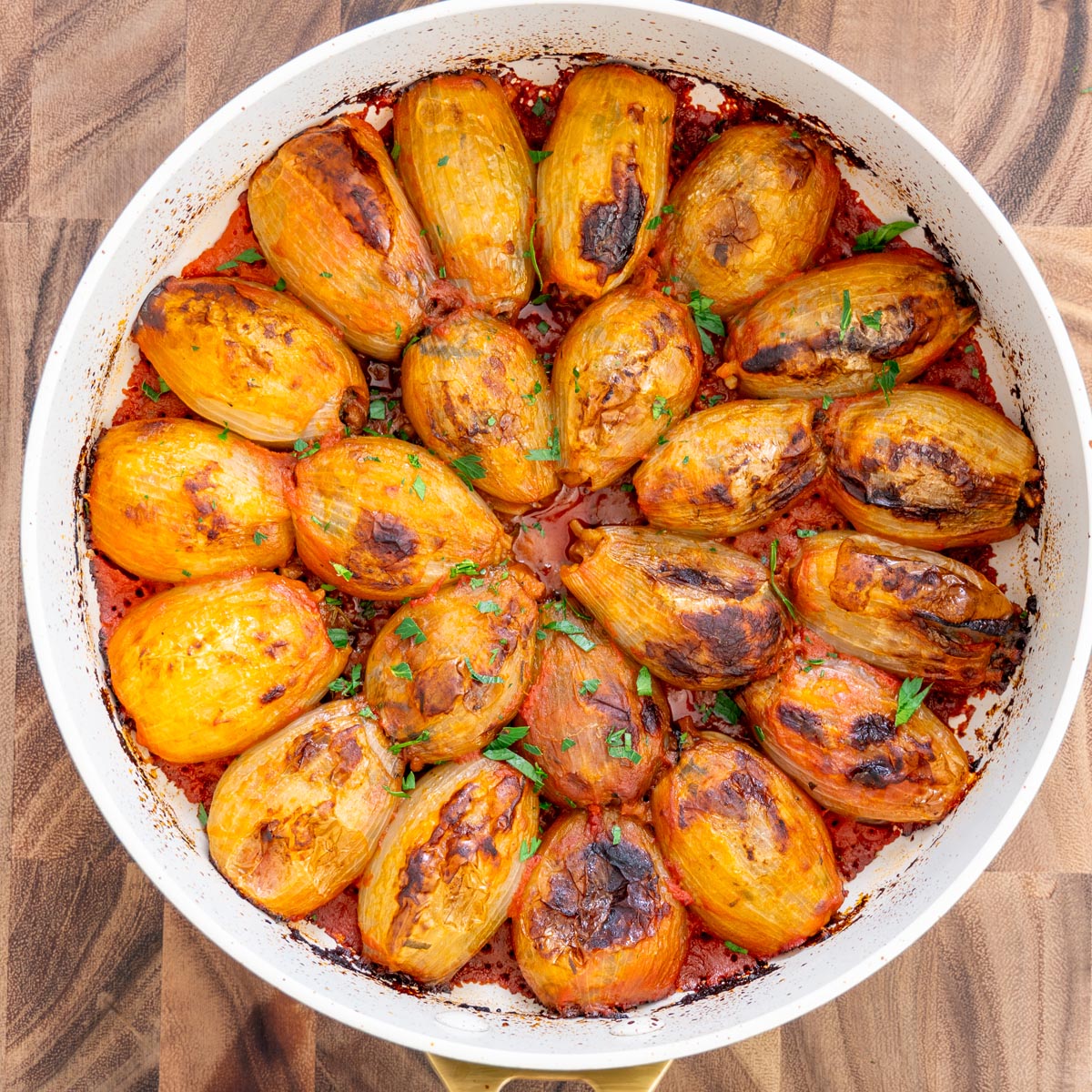 overhead view of baked stuffed onions packed into a white pan of tomato sauce.