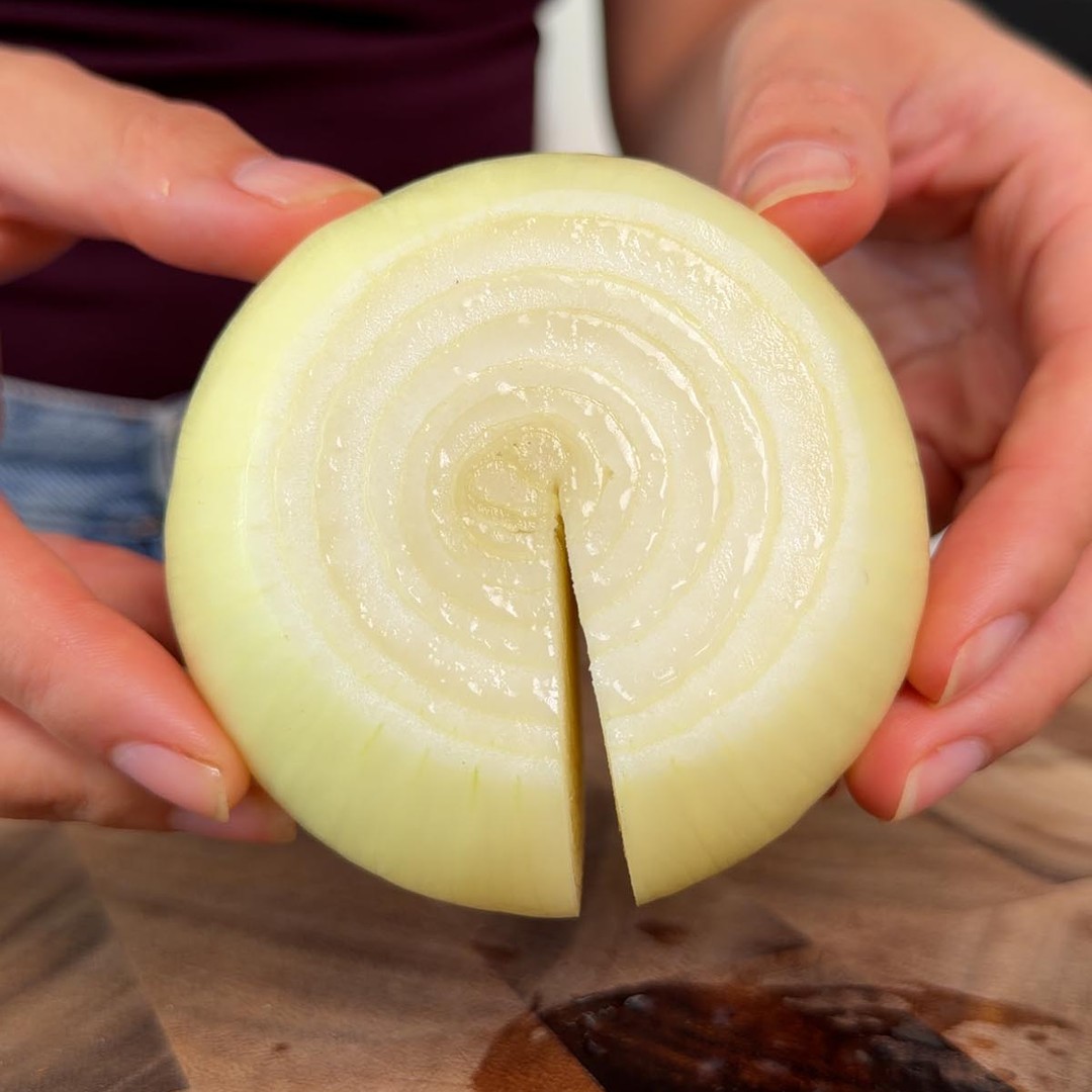 Sarah Cobacho holding a peeled yellow onion with an incision cut down one side.