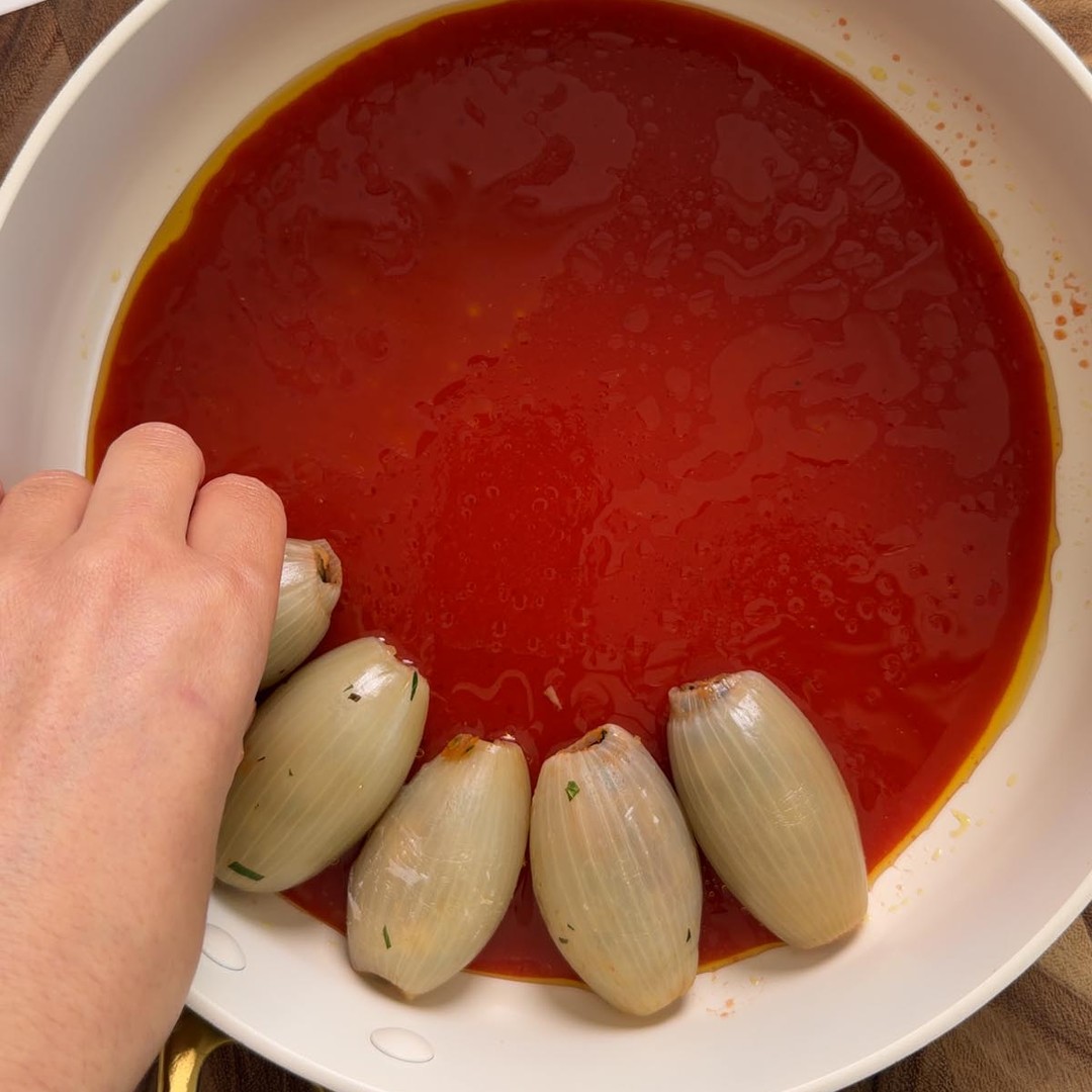 tomato sauce spread over the base of a pan with the first stuffed onion parcels arranged on top.