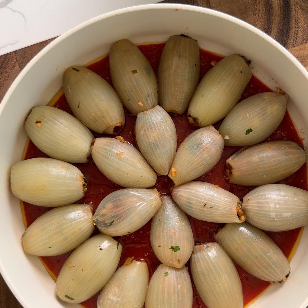 stuffed onion parcels arranged in a ring in a pan over tomato sauce.