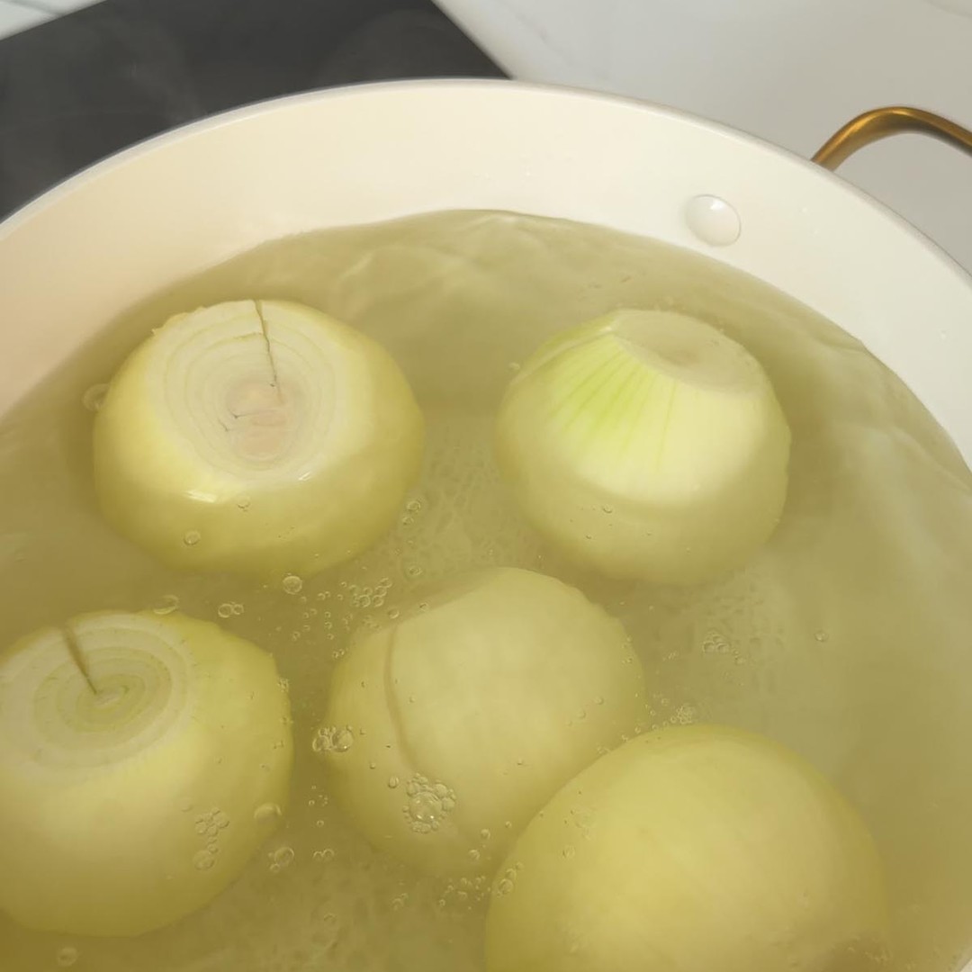 peeled yellow onions boiling in a large pot of water.