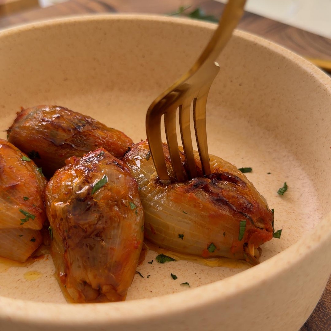 lifting a baked stuffed onion out of the pan with a fork.